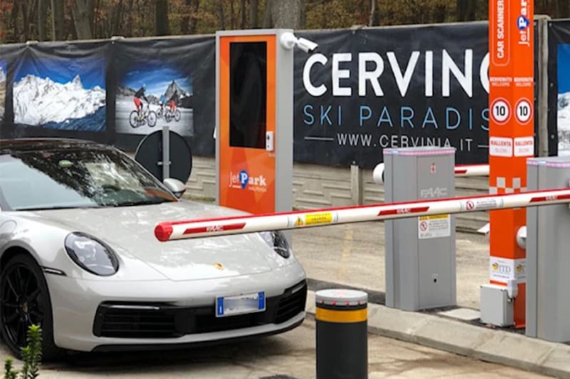 Weißer Sportwagen vor geschlossener Schranke, orange Kassenstation mit JetPark-Logo und Cervinia-Banner im Hintergrund.