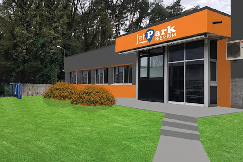 Orange-graues Bürogebäude mit JetPark Premium Schild über Glastür, Stufen, Rasenfläche und Sträuchern davor.