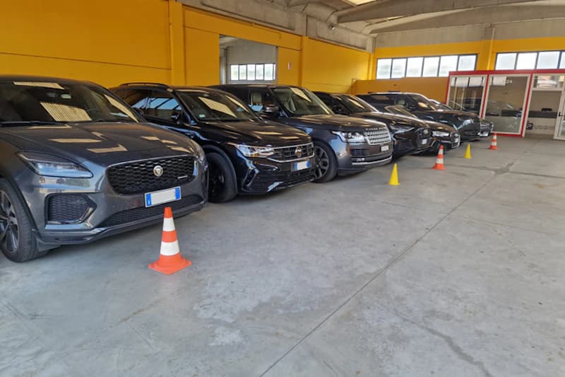 Reihe geparkter dunkler Dienstfahrzeuge in einer hellen Parkhalle mit Verkehrsleitkegeln und Büro am Ende.