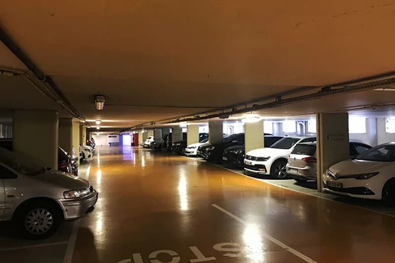 Unterirdische Parkebene mit geparkten Autos an beiden Seiten, Stützsäulen und glänzendem orangefarbenen Boden.