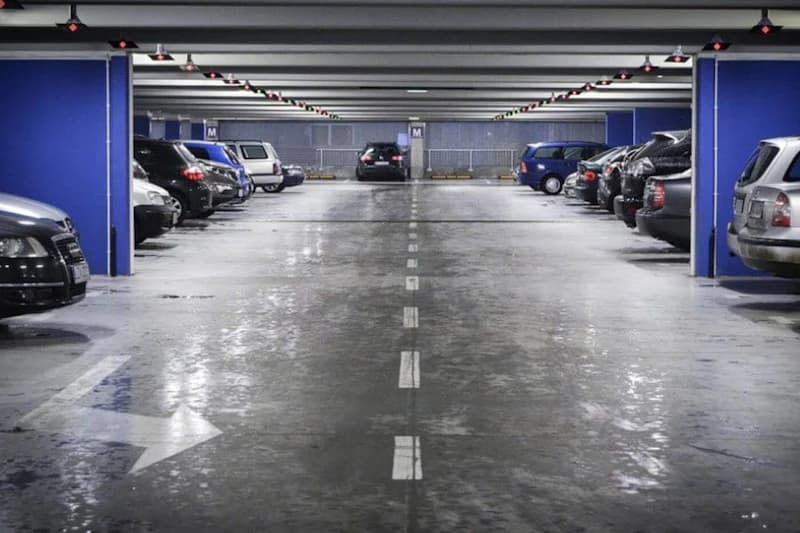 Überdachtes Parkhaus mit geparkten Autos auf beiden Seiten, blauen Stützen und Mittelspur mit Richtungspfeil.