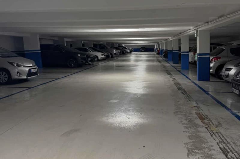 Unterirdische Parkebene mit geparkten Autos an beiden Seiten, blau markierte Säulen und glänzender Betonboden.