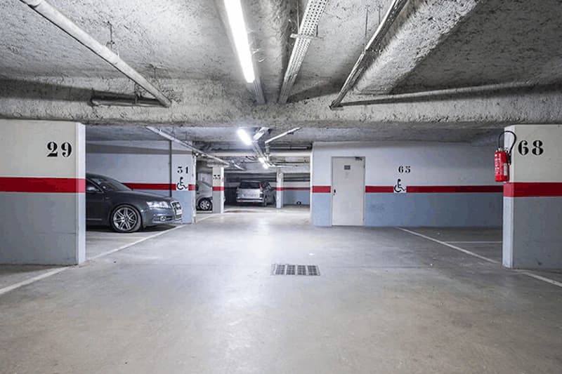 Beleuchtete Tiefgarage mit nummerierten Stellplaetzen, geparkten Autos, Rollstuhlzeichen und Feuerloescher.