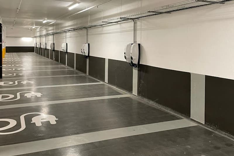 Leere überdachte Parkreihe mit markierten Stellflächen und an der Wand montierten Ladestationen.