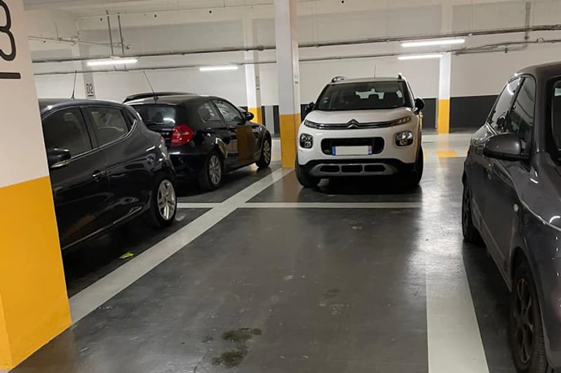 Parkhalle mit mehreren geparkten Autos, gelb markierten Säulen und markierten Stellplätzen unter Deckenbeleuchtung.