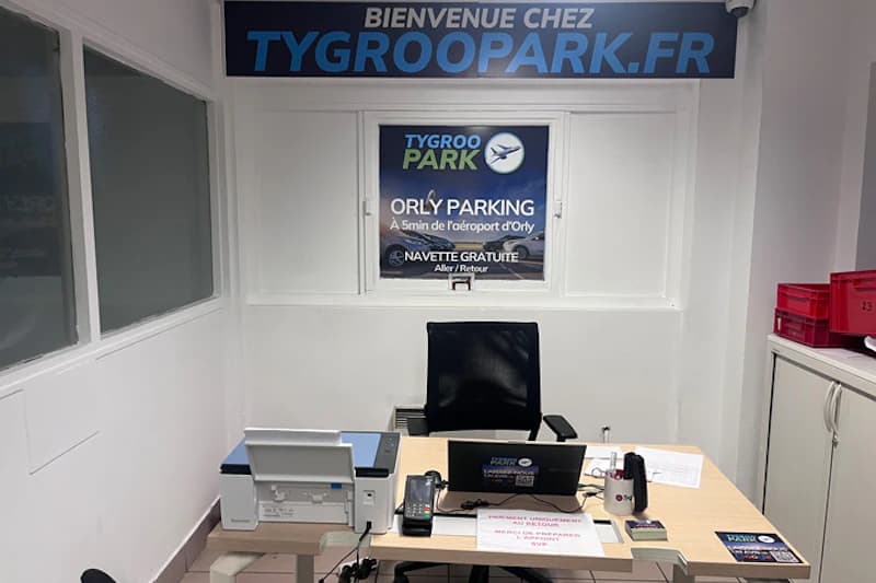 Kleines Empfangsbüro mit Schreibtisch, Drehstuhl, Laptop, Drucker und TYGROOPARK.FR Banner.