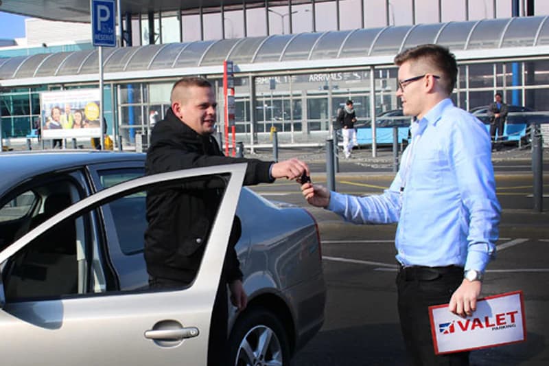 Mitarbeiter übergibt Autoschlüssel an Mann neben geöffnetem Wagen vor Terminaleingang.