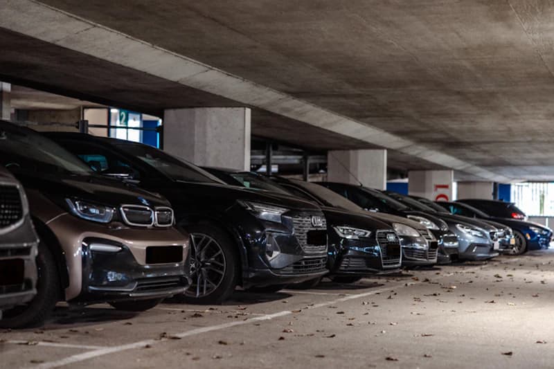 Geparkte Autos in einer niedrigen, überdachten Parkhalle mit Betonsäulen und vereinzelten Laubblättern auf dem Boden.