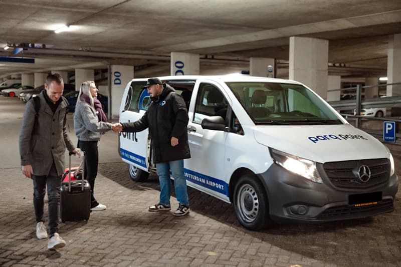 Mitarbeiter schüttelt Hand mit Passagier neben weißem Parq Point Transporter im Parkhaus.