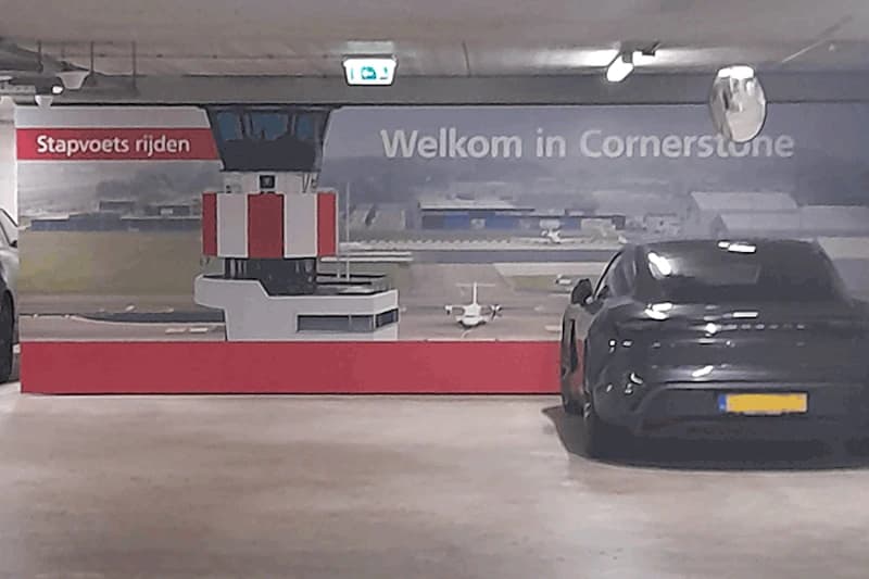 Tiefgarage mit Wandbild eines Kontrollturms und Kleinflugzeugs sowie einem geparkten schwarzen Auto rechts.