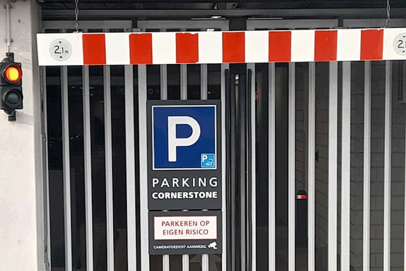 Einfahrt zur Tiefgarage mit geschlossenen Metallgittern, blaues P-Parkzeichen, Höhenbegrenzung 2,1 m und rotes Ampellicht.