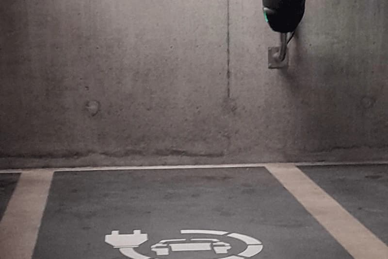 Parklücke in Tiefgarage mit E-Ladesymbol auf dem Boden und Ladestecker an einer Betonwand.