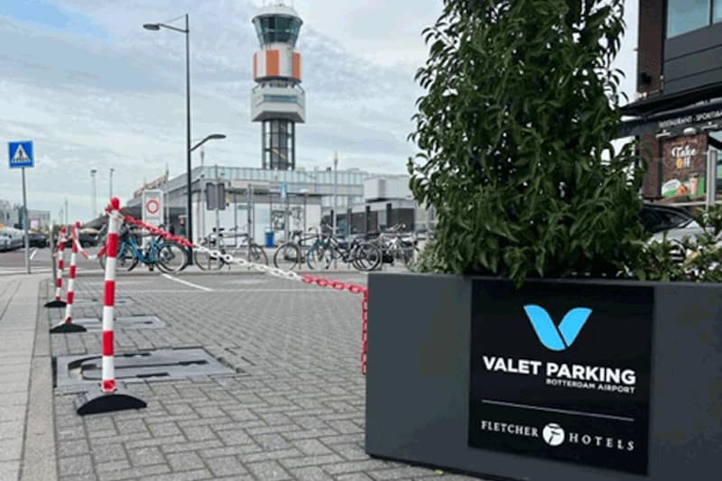 Pflanzkübel mit Valet Parking Schild und Fletcher Hotels Logo, rote Kettenabsperrung, Fahrradständer und Kontrollturm am Flughafen Rotterdam.