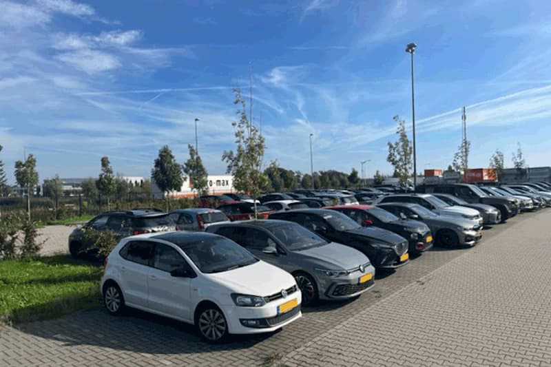 Außenparkplatz mit Reihen geparkter Autos, Straßenlaternen, Zaun und klarem Himmel.