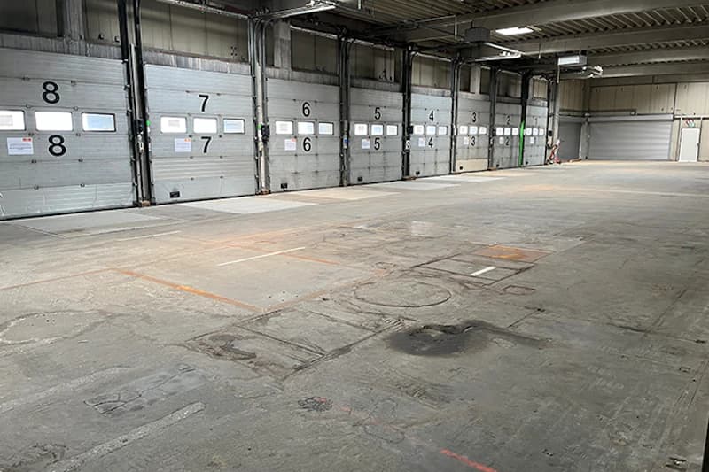 Leere Parkhalle mit nummerierten Rolltoren 3 bis 8, Betonboden und Hallendecke mit Beleuchtung.
