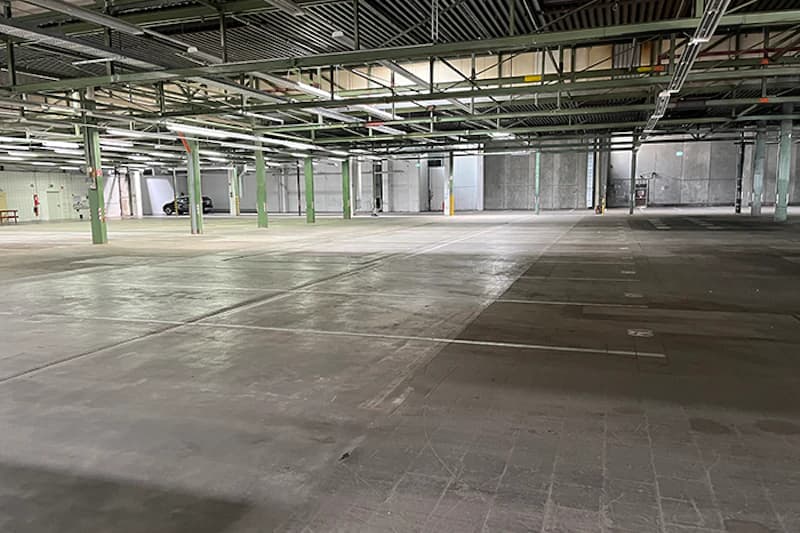 Große leere Parkhalle mit Betonboden, grünen Stützen und Deckenbeleuchtung.
