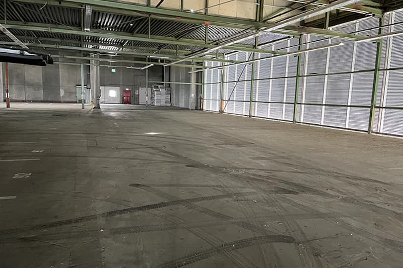 Leere Parkhalle mit Betonboden und Reifenspuren, Stahlträgern und großflächigen Lamellenfenstern rechts.