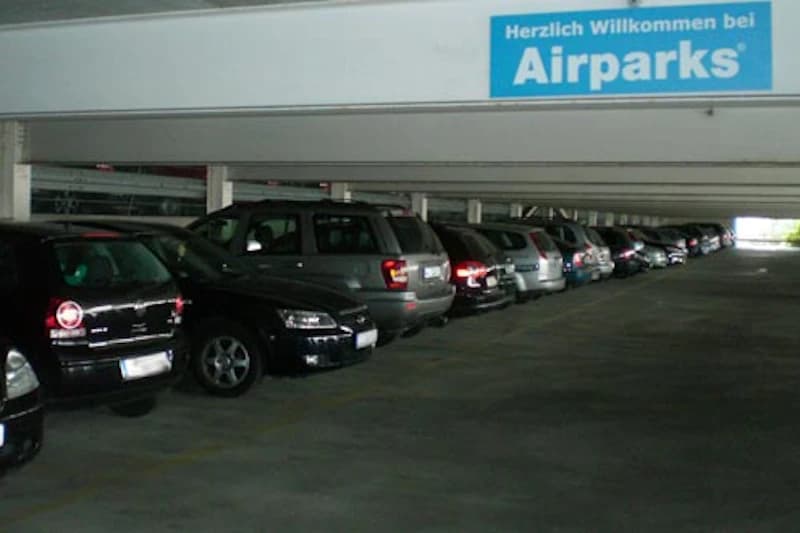 Geparkte Autos in einer dunklen Parkhausreihe unter niedriger Decke mit blauem Airparks-Schild.