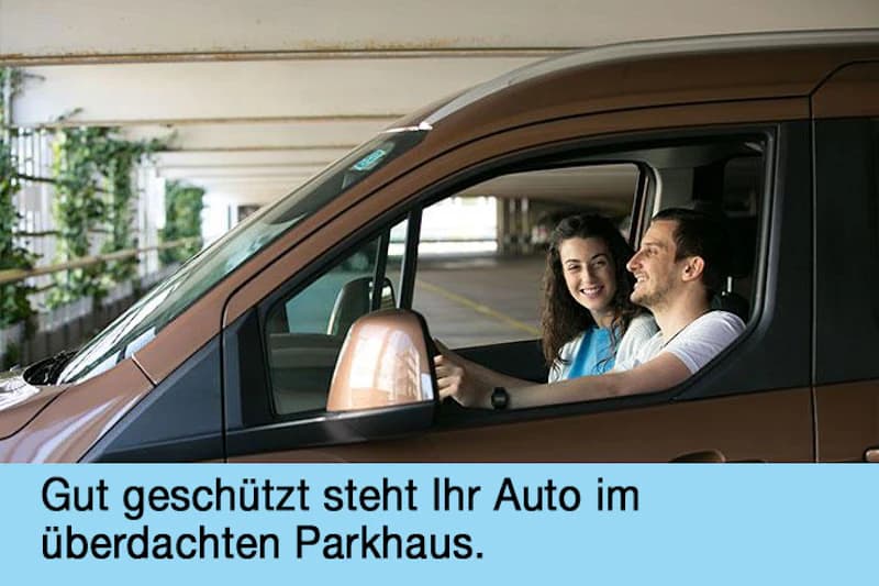 Mann am Steuer und Frau auf Beifahrersitz in braunem Auto im überdachten Parkhaus.