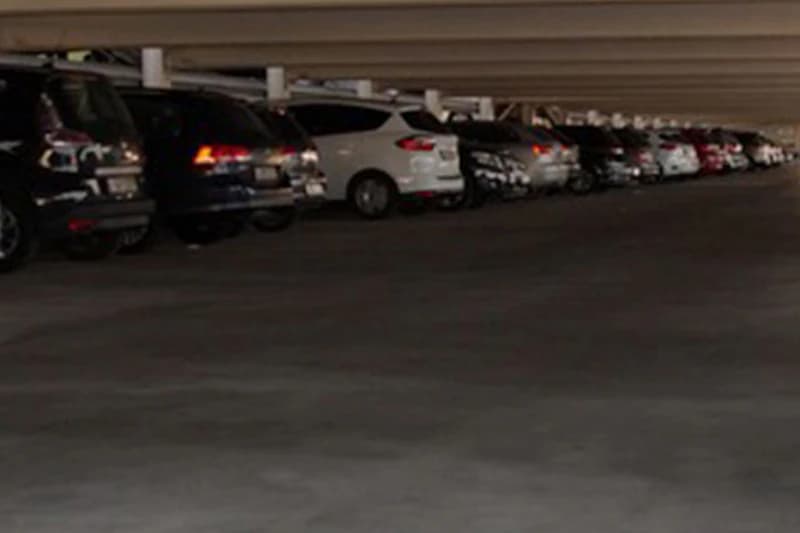 Reihe geparkter Autos in einem beleuchteten Parkhaus mit niedriger Decke und Stützen.