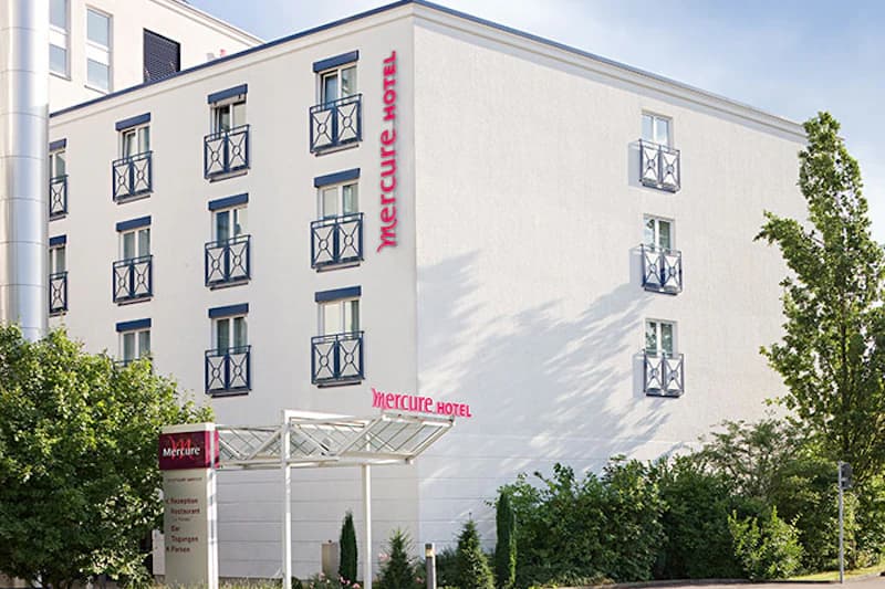 Weiße Hotelfassade mit kleinen Balkonen, Eingangsüberdachung und Mercure Hotel Schriftzug.