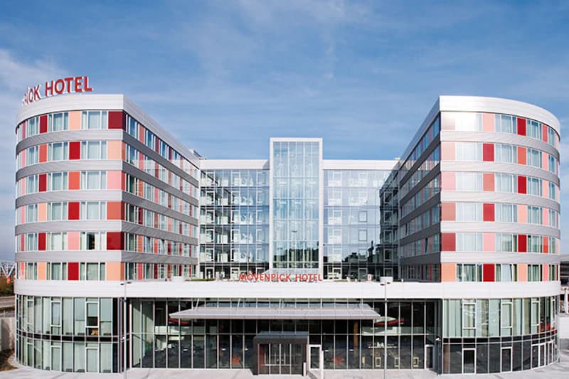 Vorderansicht des Mövenpick Hotels am Flughafen mit zwei runden Flügeln und zentraler Glasfassade.