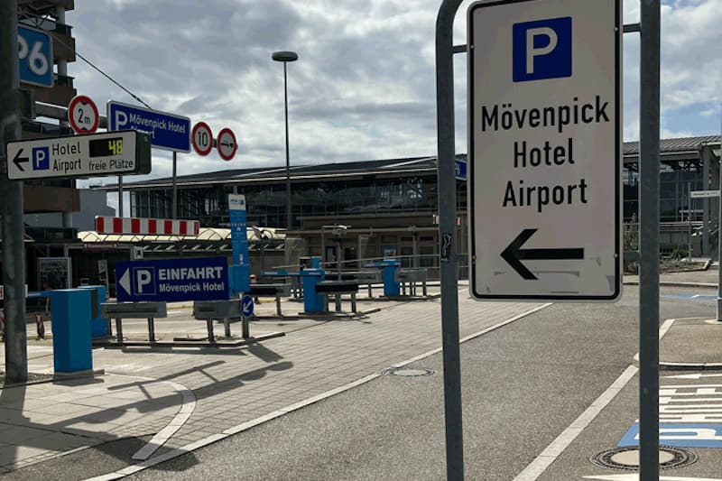 Schilder zum Mövenpick Hotel Airport und Einfahrt zum Parkplatz mit Schranken und blauem Parkleitsystem vor dem Terminal.