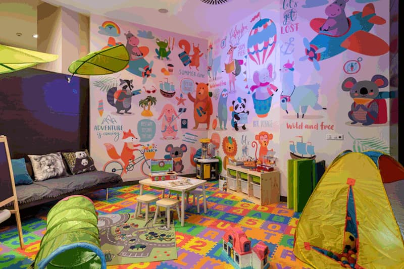 Buntes Kinderspielzimmer mit Schaumstoffbuchstabenboden, Tisch, Hocker, Spieltunnel und Spielzelt.