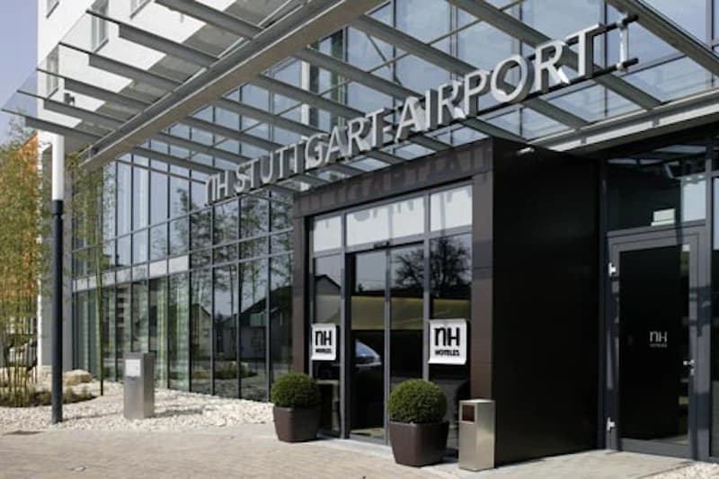Eingangsbereich des NH Stuttgart Airport mit großer Glasfassade, Vordach, Schiebetüren und zwei Pflanzenkübeln.
