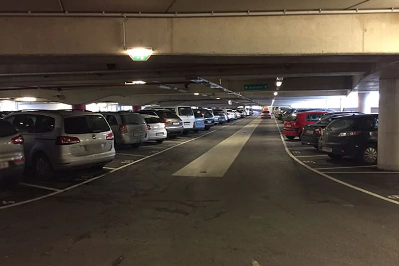 Überdachtes Parkdeck mit Reihen geparkter Fahrzeuge, Mittelgang und sichtbaren Betonsäulen.