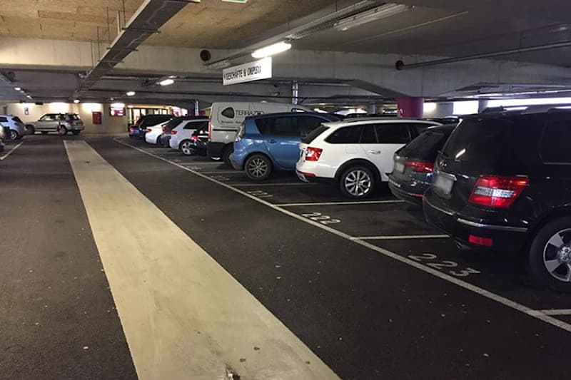 Überdachtes Parkhaus mit geparkten Autos in markierten Stellplätzen und breiter Fahrspur.