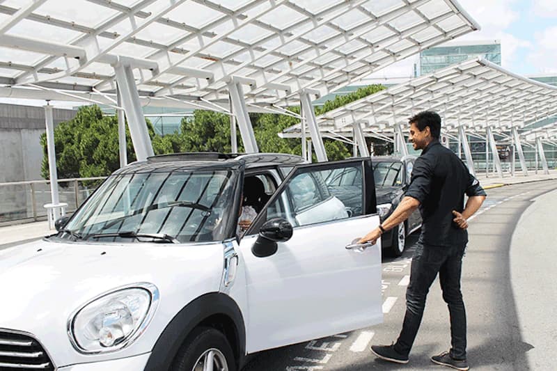 Mann öffnet die Tür eines weißen SUVs unter einer überdachten Abfahrt am Flughafen Toulouse.