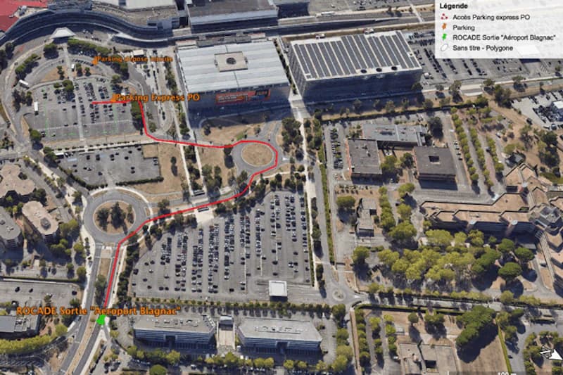 Luftaufnahme des Parkplatzes am Flughafen Toulouse mit markierter roten Route und umgebenden Gebäuden und Bäumen.