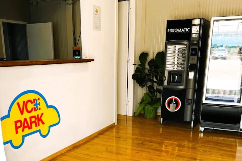 Helle Empfangstheke mit VCE PARK Autologo an Wand, Verkaufsautomat RISTOMATIC und Pflanzen auf Holzfußboden.