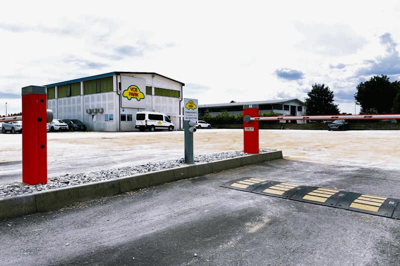 Einfahrt zu Parkgelände mit roten Schranken, Kassenstation, Bodenschwelle und Halle mit VCE Park Logo.