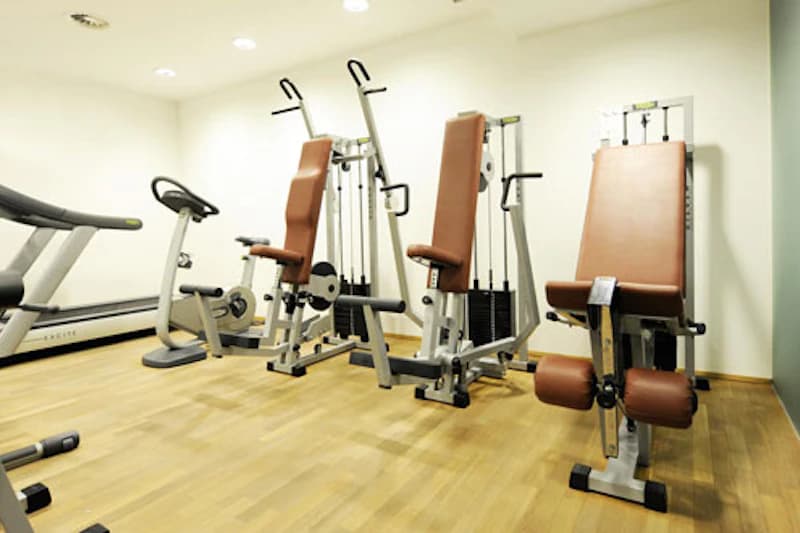 Kleiner Fitnessraum mit Kraftgeräten, Ruder- und Fahrradtrainer und Laufband auf Parkettboden.