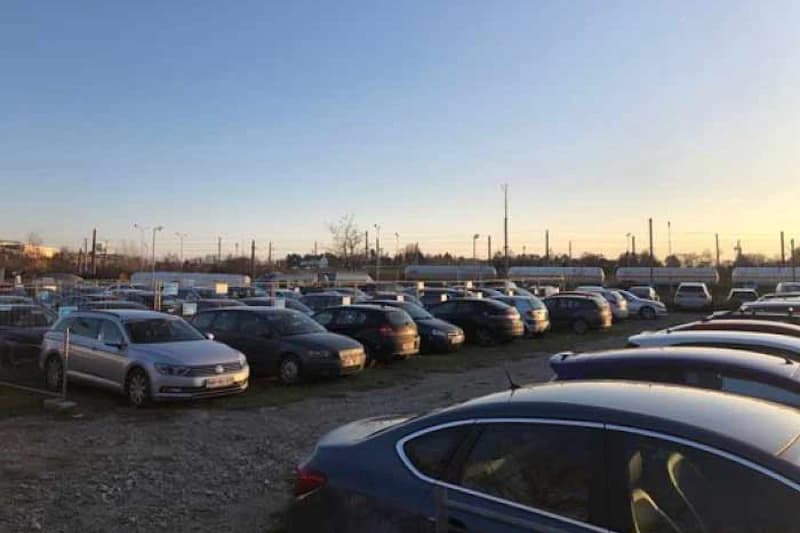 Großer, eingezäunter Außenparkplatz mit vielen geparkten Autos bei Sonnenuntergang.