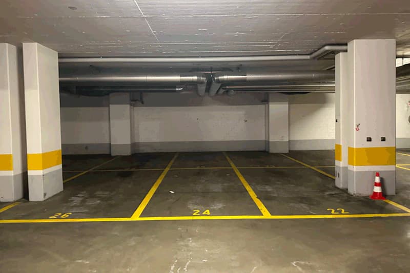 Überdachter Parkbereich in Tiefgarage mit markierten Parkfeldern 26, 24, 22, Betonpfeilern und Lüftungsrohren an der Decke.