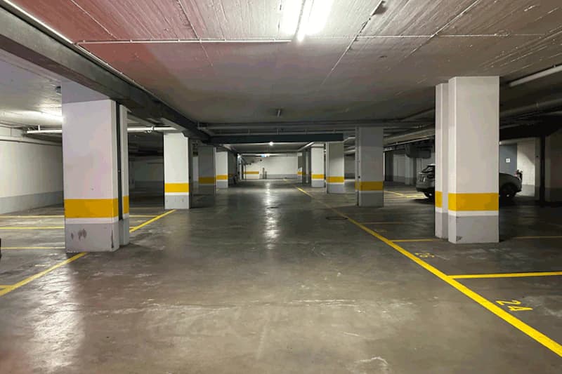 Überdachtes Parkdeck mit Betonstützen, gelben Parkmarkierungen und vereinzelten geparkten Autos.