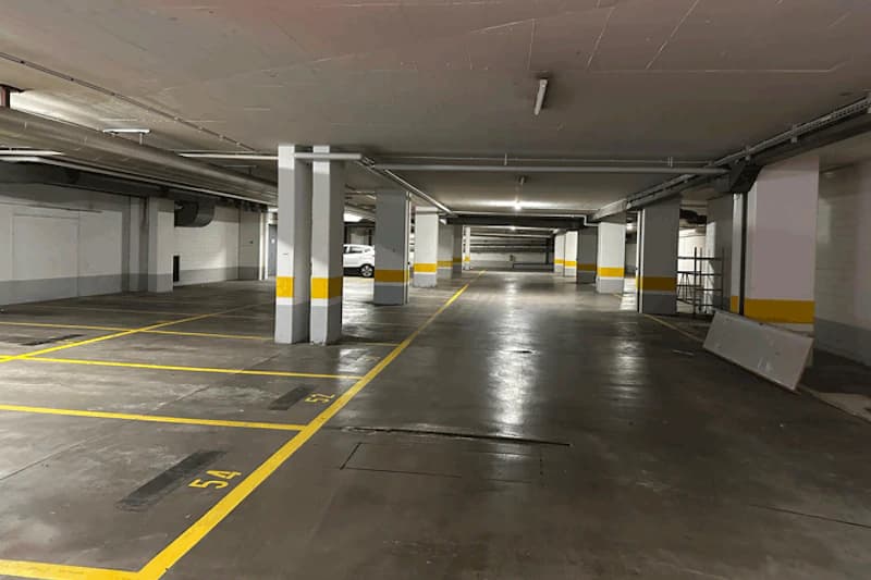 Überdachtes Parkdeck mit gelb markierten Stellplätzen, Reihen von Stützen und einem weißen Auto im Hintergrund, hell beleuchtet.